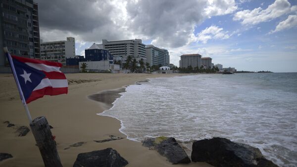 A Puerto Rican flag flies on an empty beach at Ocean Park, in San Juan, Puerto Rico, Thursday, May 21, 2020. Puerto Rico is cautiously reopening beaches, restaurants, churches, malls, and hair salons under strict conditions as the U.S. territory emerges from a two-month lockdown despite dozens of new coronavirus cases reported daily.  - Sputnik International