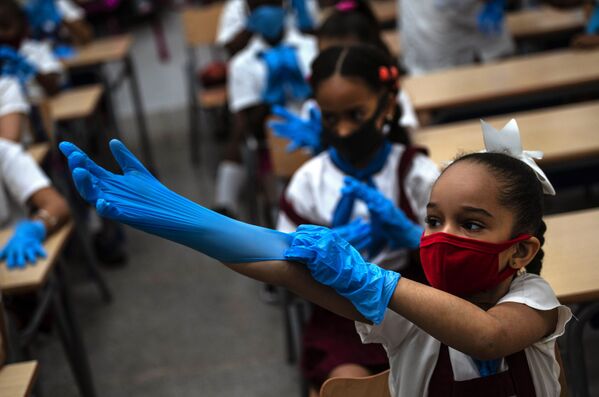 A mask-wearing student puts on plastic gloves as a precaution amid the spread of the new coronavirus during class in Havana, Cuba, 2 November 2020. Tens of thousands of school children returned to class Monday in Havana for the first time since the coronavirus pandemic prompted authorities to shut the island down in April.   - Sputnik International