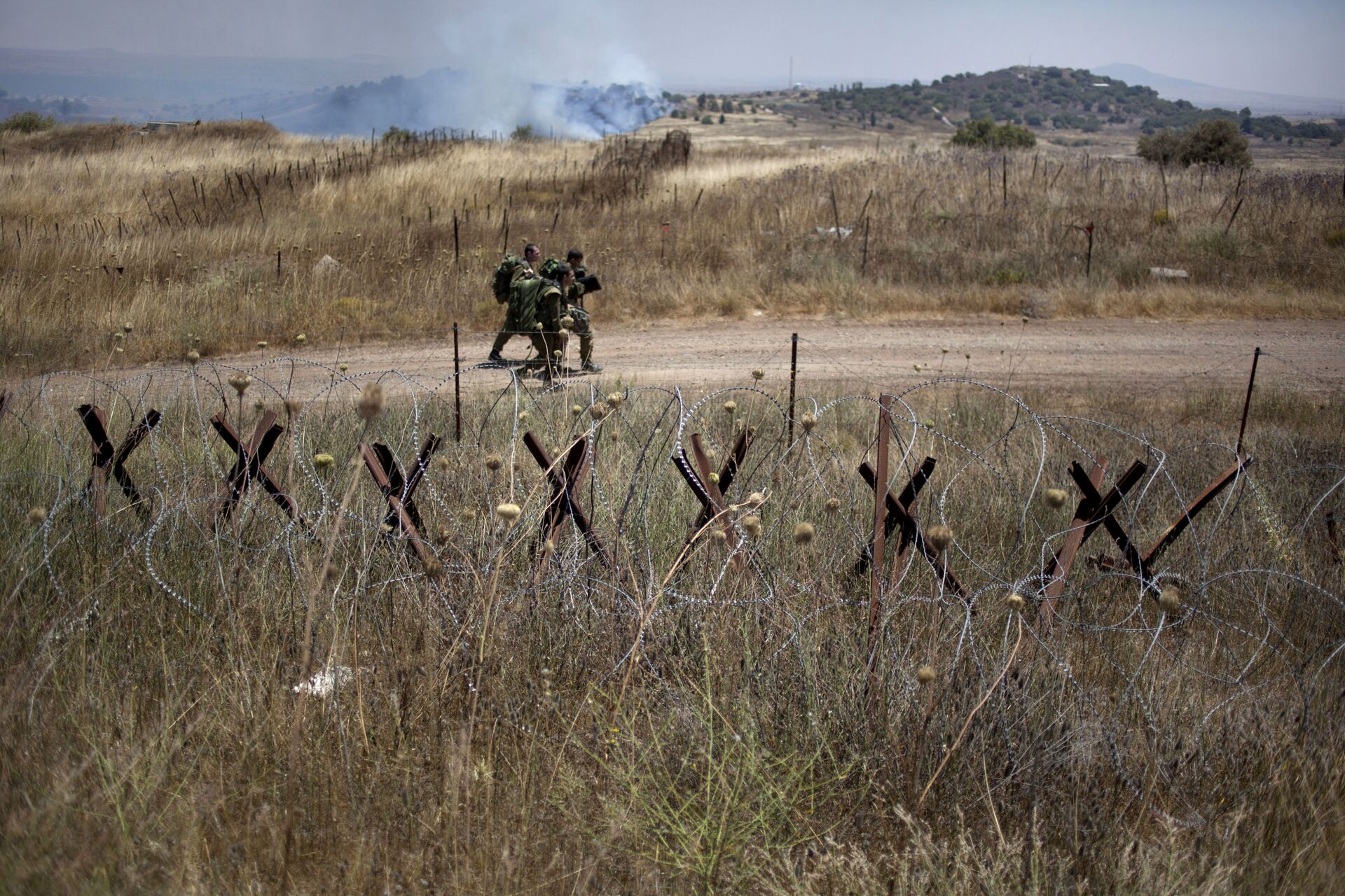 Israeli soldiers walk back from a position on the border with Syria on the Israeli controlled Golan Heights as smoke rises following explosions, Tuesday, July 16, 2013. - Sputnik International, 1920, 14.06.2023