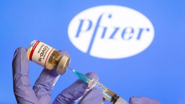 A woman holds a small bottle labelled with a Coronavirus COVID-19 Vaccine sticker and a medical syringe in front of displayed Pfizer logo in this illustration taken, October 30, 2020. - Sputnik International