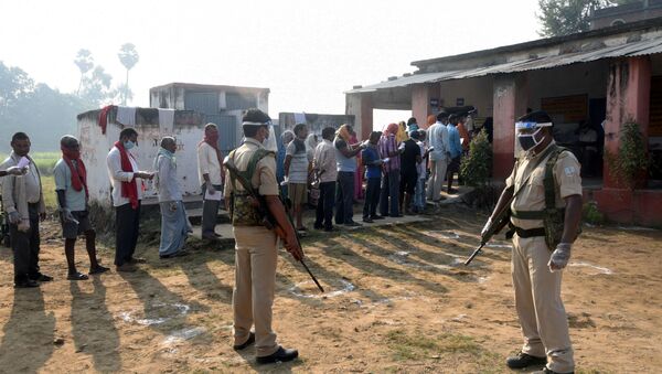 Policemen wearing protective face shields stand guard as voters stand in a queue to cast their vote outside a polling booth during the state assembly election, amidst the spread of the coronavirus disease (COVID-19), at a village on the outskirts of Patna, in the eastern state of Bihar, India, October 28, 2020 - Sputnik International