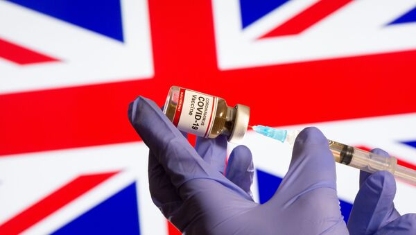 A woman holds a small bottle labeled with a Coronavirus COVID-19 Vaccine sticker and a medical syringe in front of displayed UK flag in this illustration taken, October 30, 2020 - Sputnik International