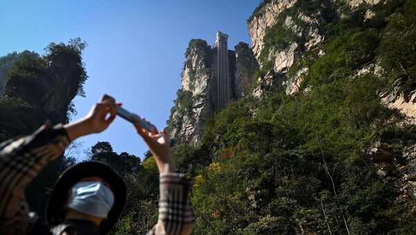 A tourist with a face mask takes a picture with her mobile phone at the entrance of the Bailong Elevator in the Zhangjiajie National Forest Park in China's Hunan province. - Sputnik International