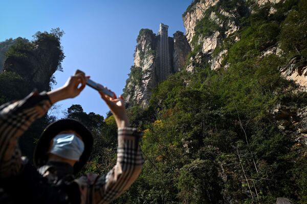 A tourist with a face mask takes a picture with her mobile phone at the entrance of the Bailong Elevator in the Zhangjiajie National Forest Park in China's Hunan province. - Sputnik International