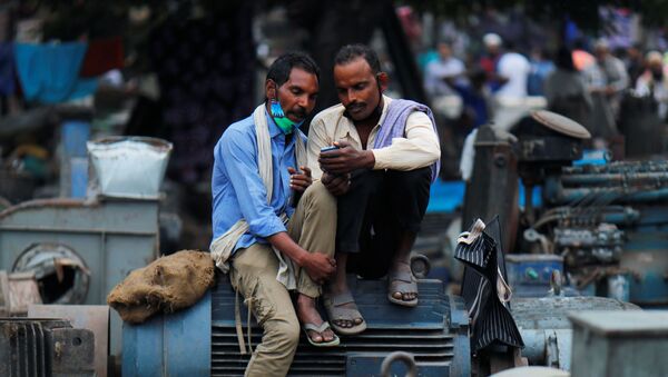 Men wearing protective face masks on their chins, amid the coronavirus disease (COVID-19) outbreak, watch a video on a mobile phone as they sit at a second-hand motor parts market in the old quarters of Delhi, India, November 16, 2020 - Sputnik International