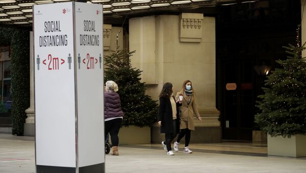 A woman wearing a face mask walks past Christmas trees and a social distancing sign outside the Selfridges department store on Oxford Street, which is temporarily closed for in-store browsing with online collection possible from a collection point, during England's second coronavirus lockdown, in London, Monday, Nov. 23, 2020 - Sputnik International