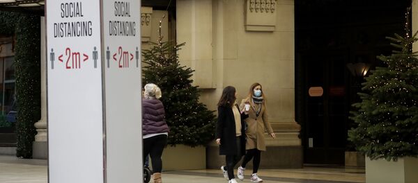 A woman wearing a face mask walks past Christmas trees and a social distancing sign outside the Selfridges department store on Oxford Street, which is temporarily closed for in-store browsing with online collection possible from a collection point, during England's second coronavirus lockdown, in London, Monday, Nov. 23, 2020 - Sputnik International