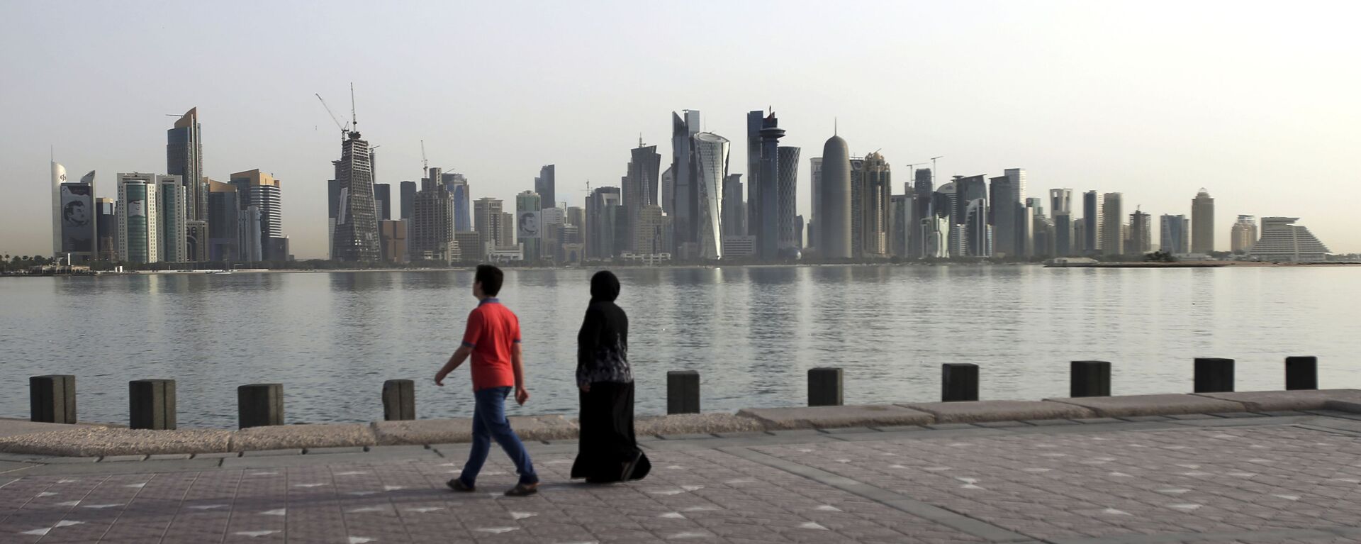 In this Friday, May 4, 2018, photo, a couple walk by the sea with the city skyline in the background, in Doha, Qatar - Sputnik International, 1920, 02.02.2021