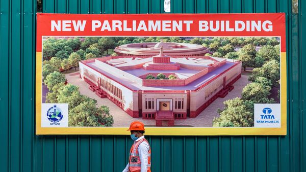 A worker walks past a banner at the boundary of the new Indian Parliament house construction site in New Delhi on December 10, 2020.  - Sputnik International
