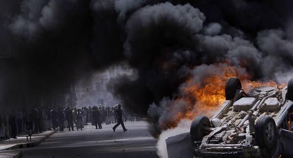 Supporters of the Yemeni government seen through the smoke of a burning vehicle that was destroyed and set on fire by anti-government demonstrators during clashes in Sanaa, Yemen, Tuesday, 22 February 2011 - Sputnik International