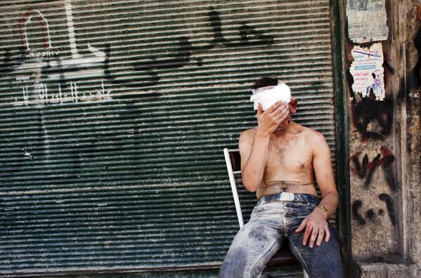 In this file photo taken on 4 September 2012, a Syrian man wounded by shelling sits on a chair outside a closed shop in the Al-Muasalat area in Aleppo - Sputnik International