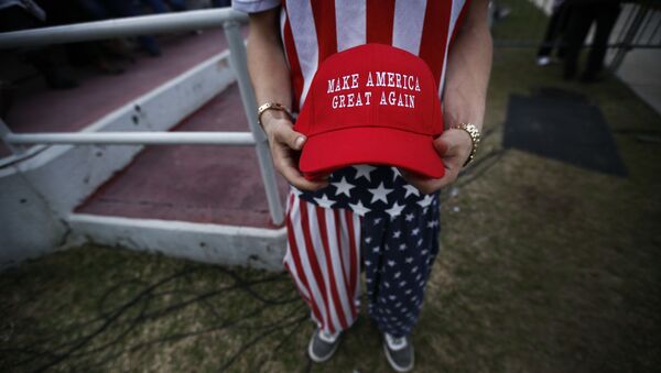 A man dressed in American flag clothes holds Make America Great Again hats before President-elect Donald Trump speaks at a rally at the Ladd–Peebles Stadium, Saturday, Dec. 17, 2016, in Mobile, Ala - Sputnik International