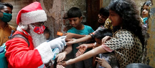 A man wearing a Santa Claus costume sanitizes children's hands inside a slum, amidst the spread of the coronavirus disease (COVID-19), in Mumbai, India, December 19, 2020 - Sputnik International