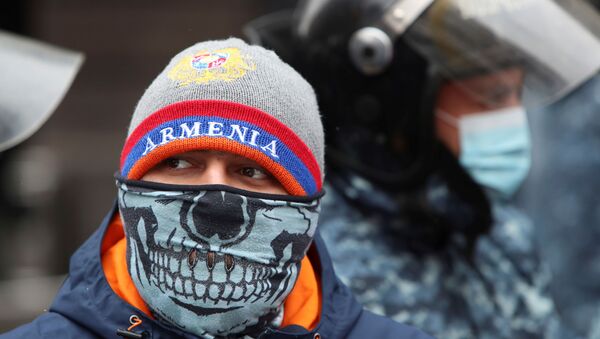 A participant wearing a face mask stands next to Armenian law enforcement officers outside the government office during an opposition rally to demand the resignation of Prime Minister Nikol Pashinyan following the signing of a deal to end a military conflict over Nagorno-Karabakh in Yerevan, Armenia December 24, 2020.  - Sputnik International