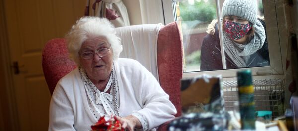 Nicky Clough looks through the window at her mother Pam Harrison opening a present on Christmas Day at Alexander House Care Home, as the spread of the coronavirus disease (COVID-19) continues, in Wimbledon, London, Britain, December 25, 2020 - Sputnik International