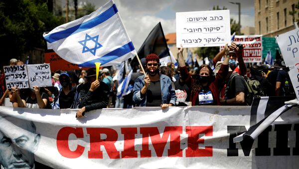 Protesters wave an Israeli flag and hold placards as they stand behind a banner reading, Crime Minister and demonstrate against Israeli Prime Minister Benjamin Netanyahu just before his corruption trial opens, outside his residence in Jerusalem May 24, 2020.  - Sputnik International