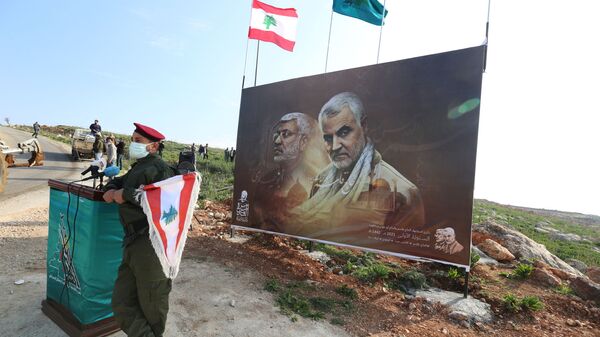 A member of Lebanon's Hezbollah holds a Lebanese flag as he stands in front of a picture depicting senior Iranian military commander General Qassem Soleimani and Iraqi militia commander Abu Mahdi al-Muhandis who were killed in a U.S. attack, during a ceremony marking the first anniversary of their killing, in the southern village of Khiam, Lebanon January 3, 2021. REUTERS/Aziz Taher - Sputnik International