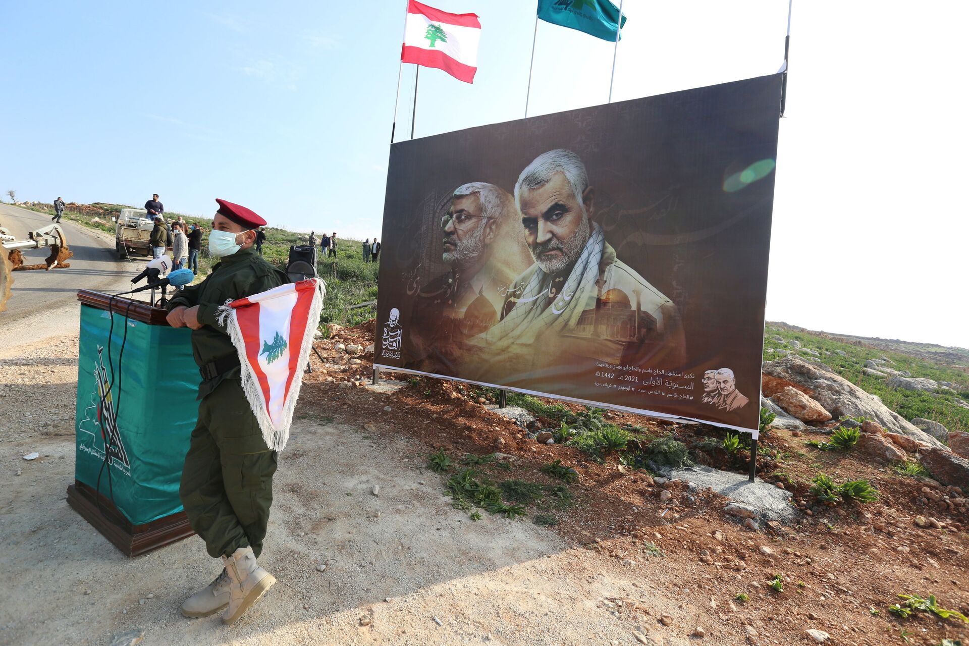 A member of Lebanon's Hezbollah holds a Lebanese flag as he stands in front of a picture depicting senior Iranian military commander General Qassem Soleimani and Iraqi militia commander Abu Mahdi al-Muhandis who were killed in a U.S. attack, during a ceremony marking the first anniversary of their killing, in the southern village of Khiam, Lebanon January 3, 2021. REUTERS/Aziz Taher - Sputnik International, 1920, 07.09.2021