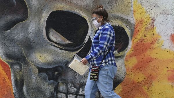 A woman wearing a face mask walks past a mural showing a skull on one of the walls of the San Nicolas Tolentino cemetery in the municipality of Iztapalapa in Mexico City on January 15, 2021, amid the COVID-19 novel coronavirus pandemic.  - Sputnik International