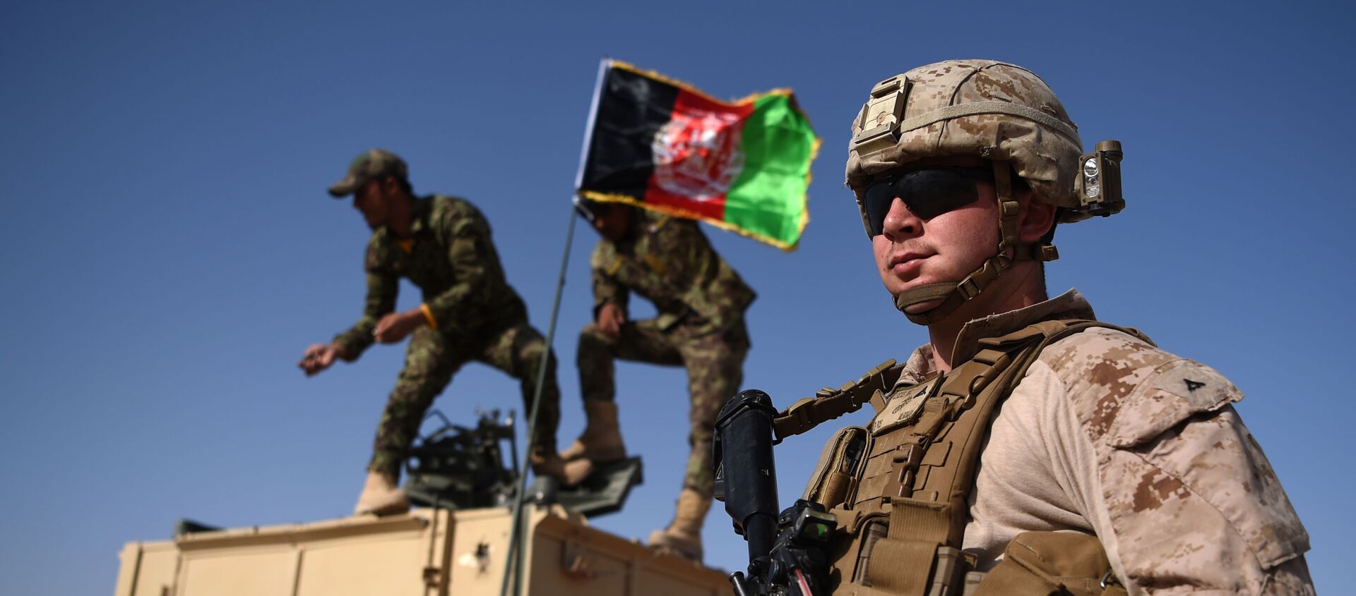 In this photograph taken on August 28, 2017, a US Marine looks on as Afghan National Army soldiers raise the Afghan National flag on an armed vehicle during a training exercise to deal with IEDs (improvised explosive devices) at the Shorab Military Camp in Lashkar Gah in Helmand province. - Marines in Afghanistan's Helmand say Donald Trump's decision to keep boots on the ground indefinitely gives them all the time in the world to retake the province, once the symbol of US intervention but now a Taliban stronghold. They may need it. At the hot, dusty Camp Shorab, where many of the recently deployed Marines train their Afghan counterparts in flat, desert terrain, the Afghans admit th - Sputnik International, 1920, 16.01.2021