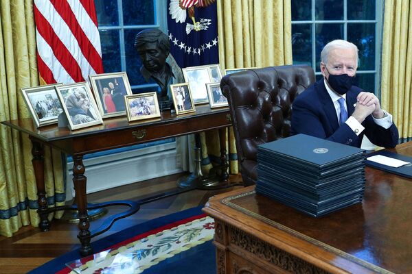 Biden family photos are displayed around a bust of activist Cesar Chavez, as US President Joe Biden prepares to sign executive orders at the Resolute Desk inside the Oval Office of the White House in Washington, US, 20 January 2021.  - Sputnik International