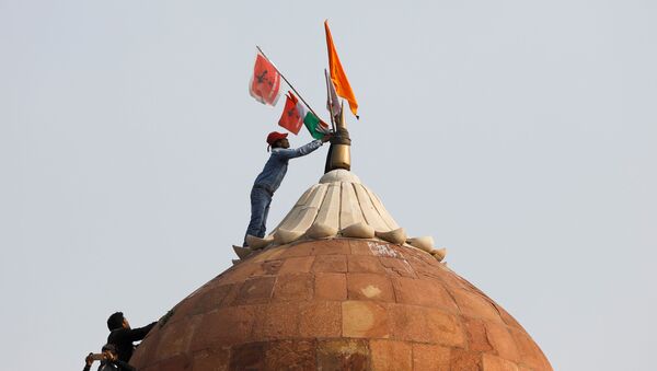 A man holds a flag as he stands on the top of the historic Red Fort during a protest against farm laws introduced by the government, in Delhi - Sputnik International