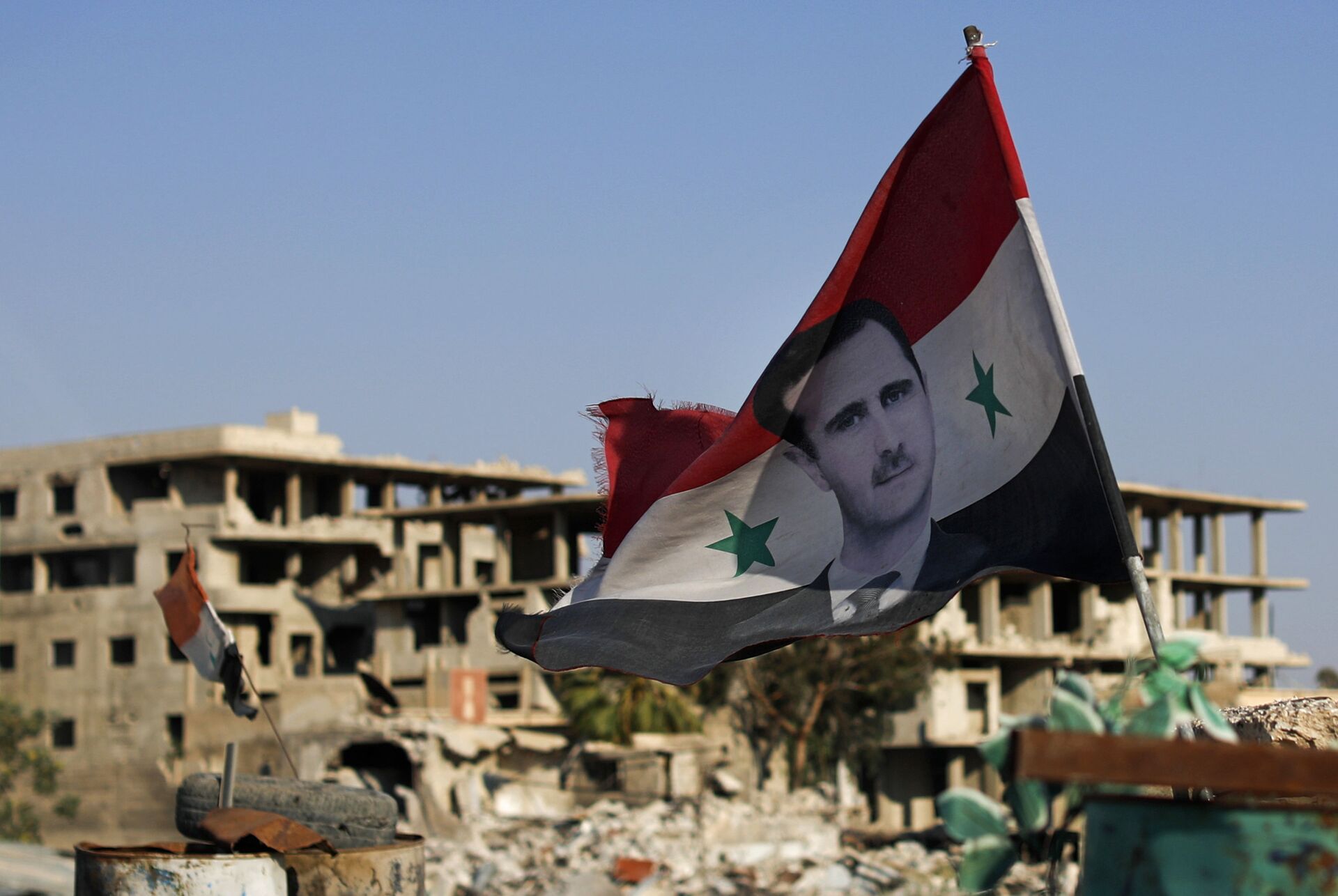 In this July 15, 2018 file photo, a Syrian national flag with a picture of Syrian President Bashar Assad flies at an Army check point, in the town of Douma in the eastern Ghouta region, near Damascus, Syria. - Sputnik International, 1920, 21.09.2022