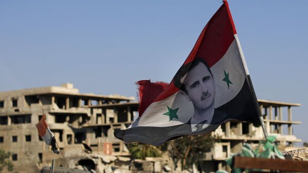 In this July 15, 2018 file photo, a Syrian national flag with a picture of Syrian President Bashar Assad flies at an army check point in the town of Douma in the eastern Ghouta region near Damascus, Syria. - Sputnik International