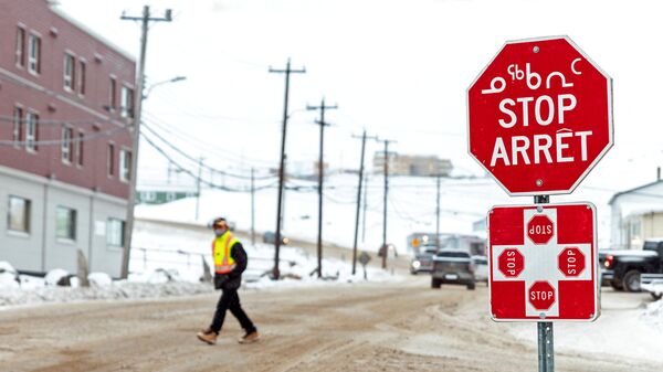 A man wearing a mask to help slow the spread of coronavirus disease (COVID-19) passes a stop sign written in English, French and Inuktitut as the territory of Nunavut enters a two week mandatory restriction period in Iqaluit, Nunavut, Canada 18 November 2020. - Sputnik International