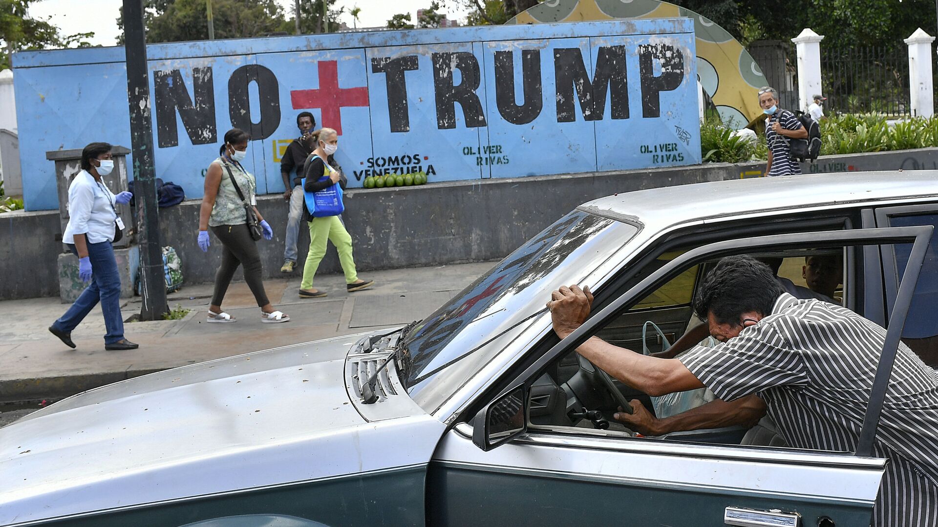 A man pushes his car that ran out of gas as people wearing protective face masks as a precaution against the spread of the new coronavirus, walk past a mural with a message that reads in Spanish:  No more Trump in Caracas, Venezuela, Sunday, Nov. 8, 2020. Venezuelan President Nicolas Maduro has sent a congratulatory message to U.S. President-elect Joe Biden who won the U.S. presidential election, defeating incumbent Donald Trump. - Sputnik International, 1920, 17.03.2021
