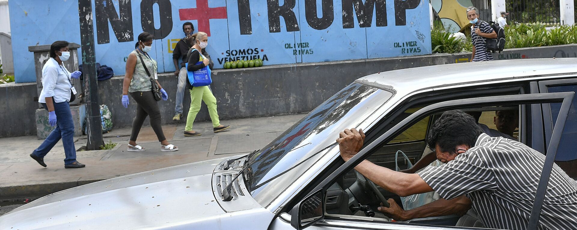A man pushes his car that ran out of gas as people wearing protective face masks as a precaution against the spread of the new coronavirus, walk past a mural with a message that reads in Spanish:  No more Trump in Caracas, Venezuela, Sunday, Nov. 8, 2020. Venezuelan President Nicolas Maduro has sent a congratulatory message to U.S. President-elect Joe Biden who won the U.S. presidential election, defeating incumbent Donald Trump. - Sputnik International, 1920, 19.01.2025