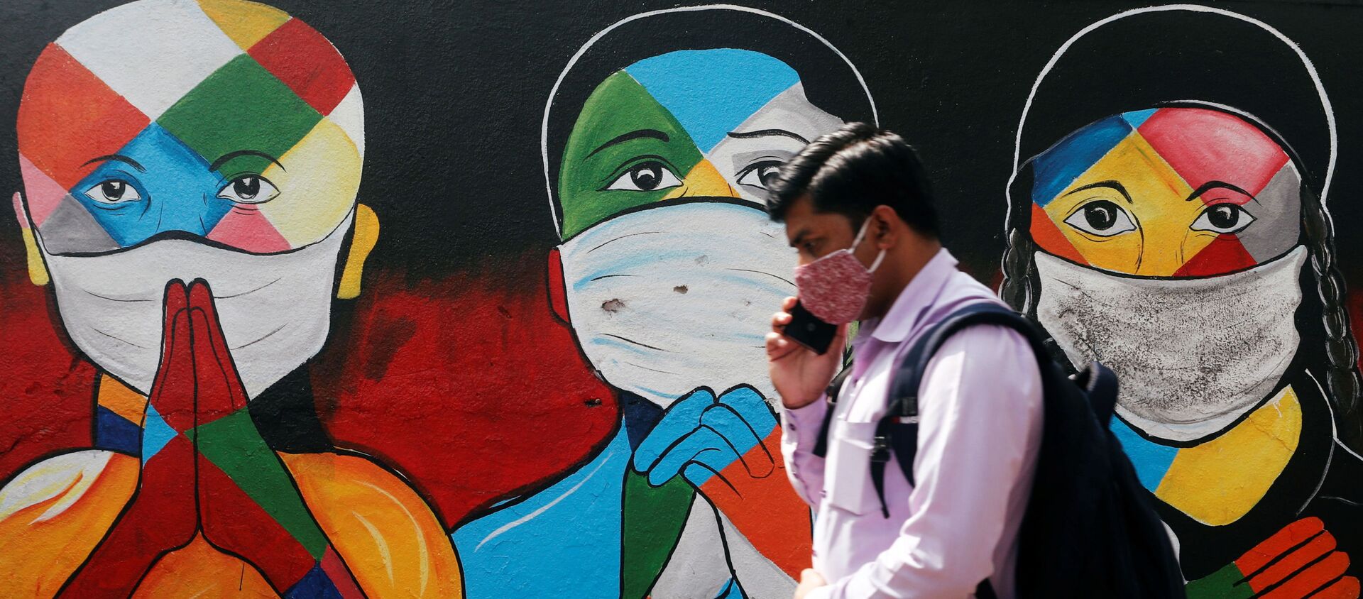 A man walks past a graffiti of people wearing protective masks amidst the spread of the coronavirus disease (COVID-19) on a street in Navi Mumbai, India - Sputnik International, 1920
