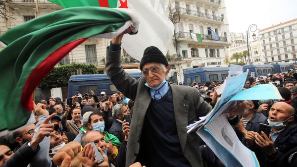 A demonstrator carries a national flag during a protest to mark the second anniversary of a mass protest movement demanding political change, in Algiers, Algeria February 22, 2021 - Sputnik International