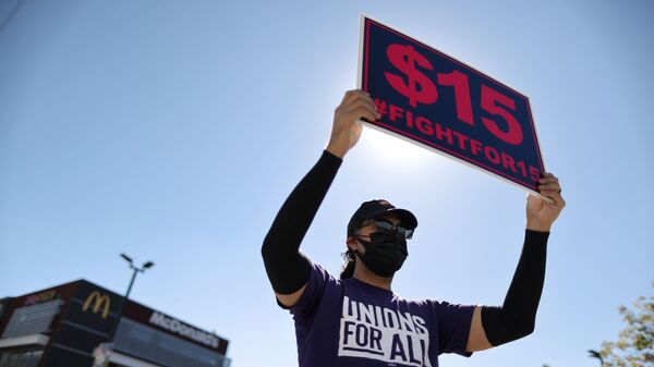 A man holds up a minimum wage sign at a rally held by fast food workers and supporters to celebrate the California Labor Commissioner’s order for the company to rehire and compensate workers who went on strike for coronavirus disease (COVID-19) protections, in Los Angeles, California, U.S., February 18, 2021. - Sputnik International