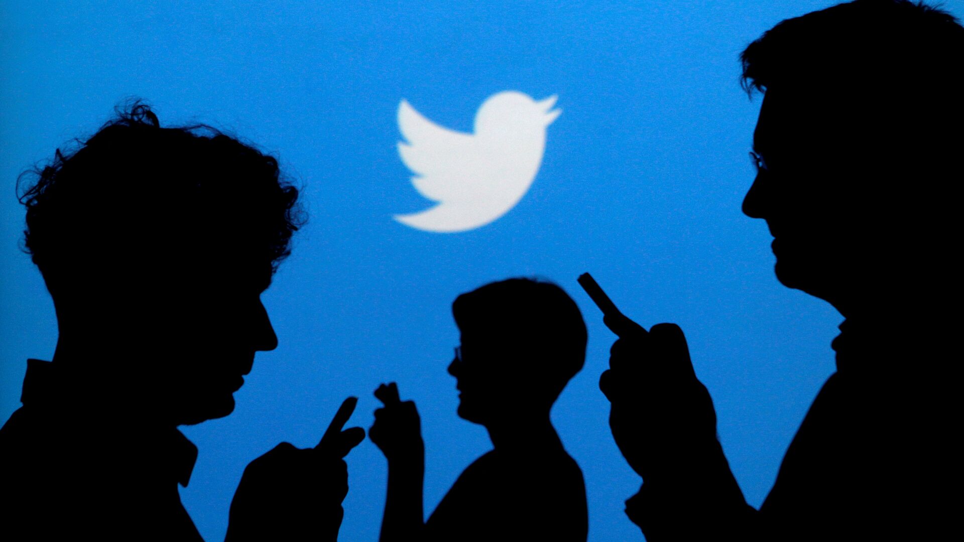 People holding mobile phones are silhouetted against a backdrop projected with the Twitter logo in this illustration picture taken September 27, 2013 - Sputnik International, 1920, 05.10.2021