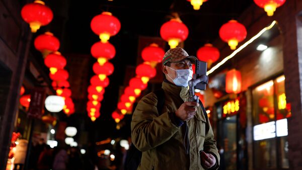 A man wearing a face mask following an outbreak of the coronavirus disease (COVID-19) uses his phone while walking near the Qianmen street ahead of Lunar New Year celebrations, in Beijing, China February 10, 2021 - Sputnik International
