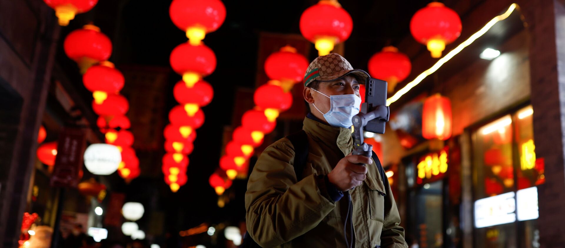 A man wearing a face mask following an outbreak of the coronavirus disease (COVID-19) uses his phone while walking near the Qianmen street ahead of Lunar New Year celebrations, in Beijing, China February 10, 2021 - Sputnik International, 1920, 02.03.2021