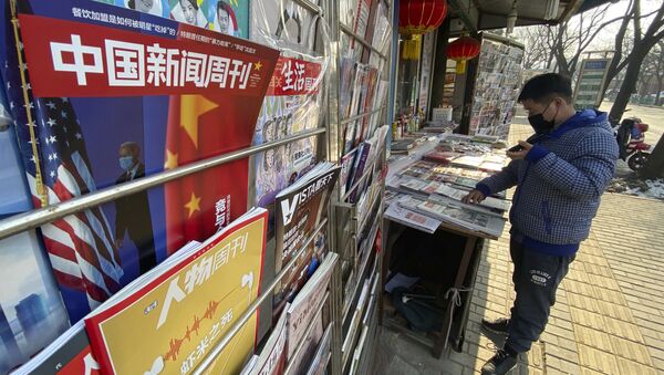 A newsstand vendor looks through his display near a magazine with a cover depicting U.S. President Joe Biden near U.S. and Chinese flags in Beijing on Thursday, Jan. 21, 2021 - Sputnik International
