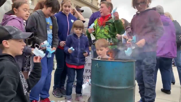 Screenshot capture the weekend demonstration in which parents and guardians encouraged children to remove their masks and throw them into the fire. The demonstration came after state lawmakers passed a measure through the House of Representatives that ban a mask mandate from being implemented in the future. - Sputnik International