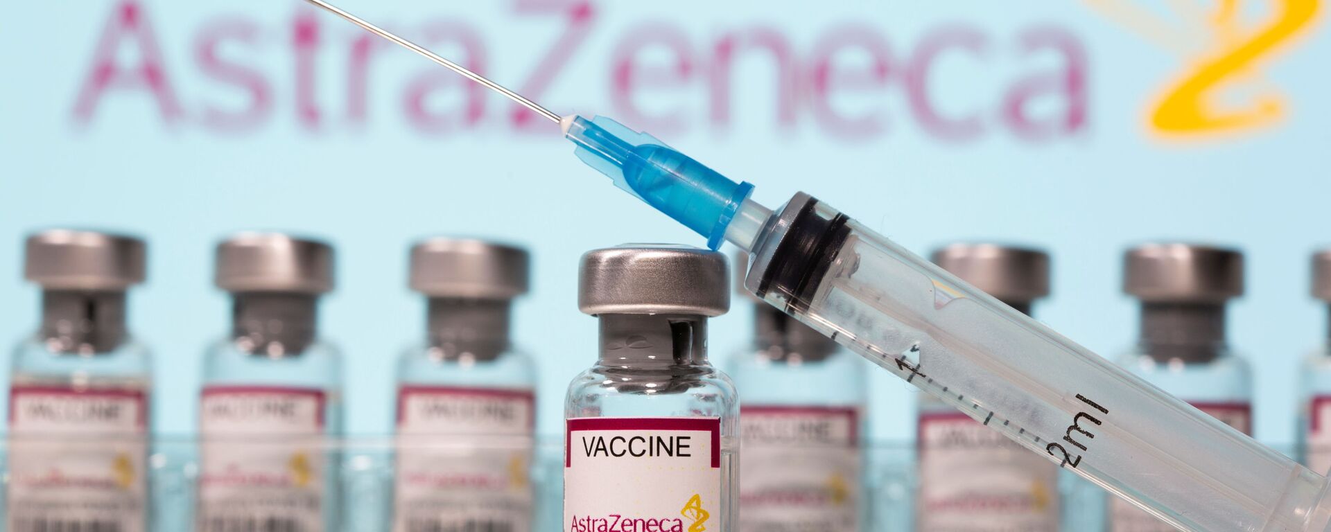 Vials labelled AstraZeneca COVID-19 Coronavirus Vaccine and a syringe are seen in front of a displayed AstraZeneca logo in this illustration taken March 10, 2021. REUTERS/Dado Ruvic/Illustration - Sputnik International, 1920, 12.04.2021