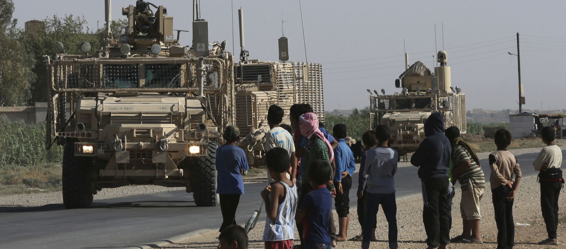  In this July 26, 2017 file photo, Syrian children and youths gather on a street as they look at a U.S. armored vehicle convoy pass on a road that links to Raqqa, northeast Syria. - Sputnik International, 1920, 14.03.2021