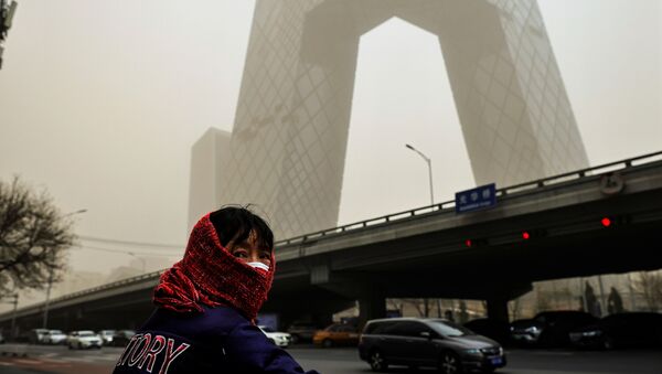 A woman wearing a head covering is seen in front of the headquarters of China's state media broadcaster CCTV that is shrouded in a haze after a sandstorm in the Central Business District of Beijing, China. - Sputnik International