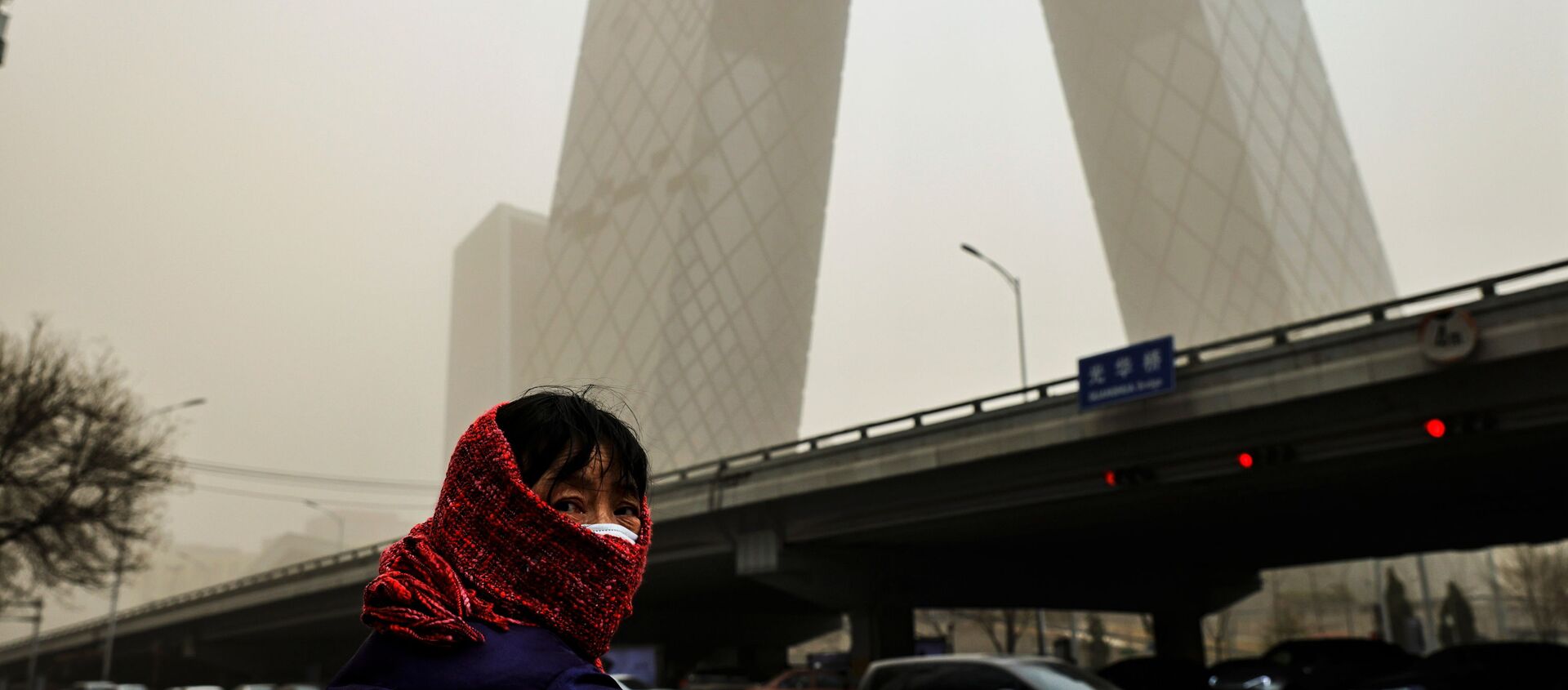 A woman wearing a head covering is seen in front of the headquarters of China's state media broadcaster CCTV that is shrouded in a haze after a sandstorm in the Central Business District of Beijing, China. - Sputnik International, 1920, 15.03.2021