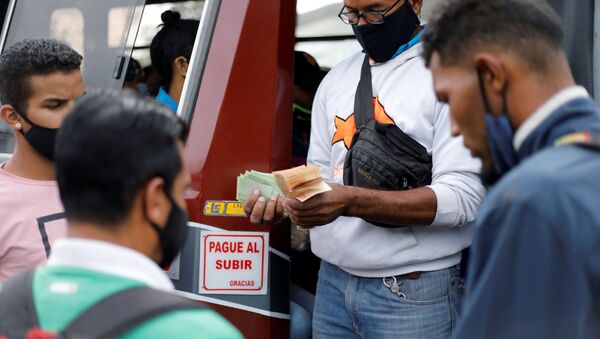 A bus driver's assistant collects fares while holding a wad of Bolivar banknotes at a bus stop outside the Antimano metro station in Caracas, Venezuela, March 9, 2021. Picture taken March 9, 2021. REUTERS/Leonardo Fernandez Viloria  - Sputnik International