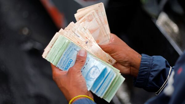 A bus driver's assistant counts a wad of Bolivar banknotes at a bus stop outside the Antimano metro station in Caracas, Venezuela, March 9, 2021. Picture taken March 9, 2021. REUTERS/Leonardo Fernandez Viloria - Sputnik International