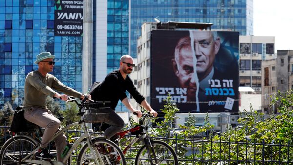 People cycle next to a Blue and White party election campaign banner depicting its leader, Israeli Defence Minister Benny Gantz, alongside Israeli Prime Minister Benjamin Netanyahu ahead of the March 23 ballot, in Tel Aviv, Israel March 17, 2021.  - Sputnik International