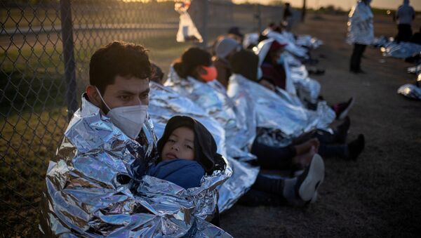 Dustin, an asylum-seeking migrant from Honduras, holds his six-year-old son Jerrardo, 6, as they awake at sunrise next to others who took refuge near a baseball field after crossing the Rio Grande river into the United States from Mexico on rafts, in La Joya, Texas, U.S., March 19, 2021. Emergency blankets were provided to the group of about 150 migrants from Central America by the U.S. Border Patrol agents.  - Sputnik International