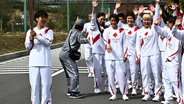 Japanese torchbearer Azusa Iwashimizu (L), a member of the Japan women's national football team, holds an Olympic Torch after passing the flame to the next torchbearer during the torch relay grand start at the J-Village National Training Centre in Naraha town, Fukushima Prefecture, Japan March 25, 2021.  - Sputnik International