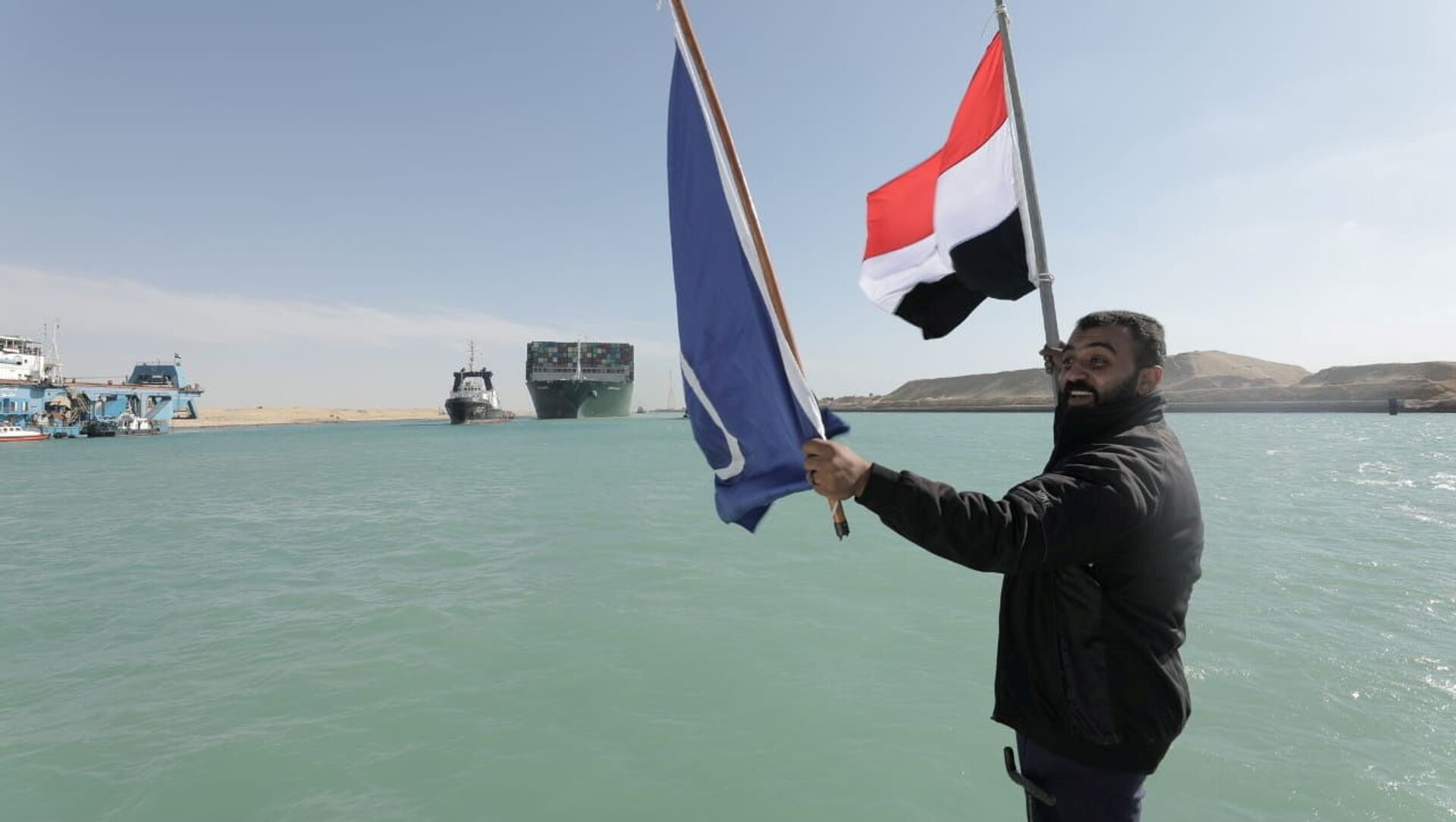 A man waves an Egyptian flag as the Ever Given, one of the world's largest container ships, is seen after it was fully floated in the Suez Canal, Egypt 29 March 2021. - Sputnik International, 1920, 30.03.2021
