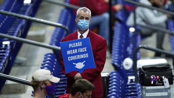 In this March 21, 2021, file photo, an usher holds a sign reminding fans to wear masks during a college basketball game between Houston and Rutgers in the second round of the NCAA tournament at Lucas Oil Stadium in Indianapolis - Sputnik International